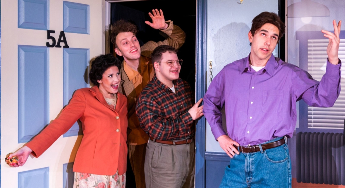 Actors in Singfeld dressed as Elaine, Kramer, George, and Jerry from the tv show "Seinfeld." The Elaine, Kramer, and George actors are leaning through a door smiling while the Jerry actor looks exasperated.